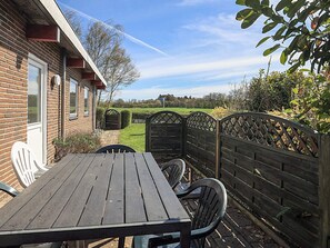 A wooden table and chairs outside a brick building with a view of a green field and a fence. - 10 Person Holiday Home in Spottrup (Spøttrup)