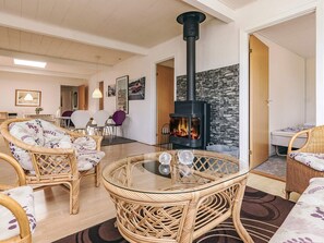 A living room with wicker furniture, a glass table, a black wood-burning stove, and a stone wall. - 10 Person Holiday Home in Spottrup (Spøttrup)