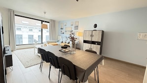 Una sala de estar moderna con un sofá, una mesa de comedor con sillas, un armario y un ventanal con vistas a edificios.