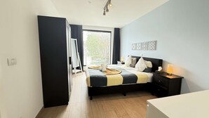 Un dormitorio con cama, mesita de noche, lámpara y vistas al exterior.
