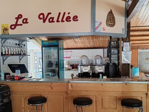 A bar area with a sign reading 'La Vallée,' a refrigerated display case, and a counter with stools. - Mobile home - 2 guests (La Tour-d'Auvergne)