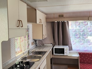 A compact kitchenette with a sink, stove, microwave, and cabinets. - Mobile home - 2 guests (La Tour-d'Auvergne)