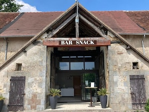 Un edificio de piedra con un cartel que dice 'BAR SNACK' sobre la entrada, plantas en macetas y un cielo despejado.