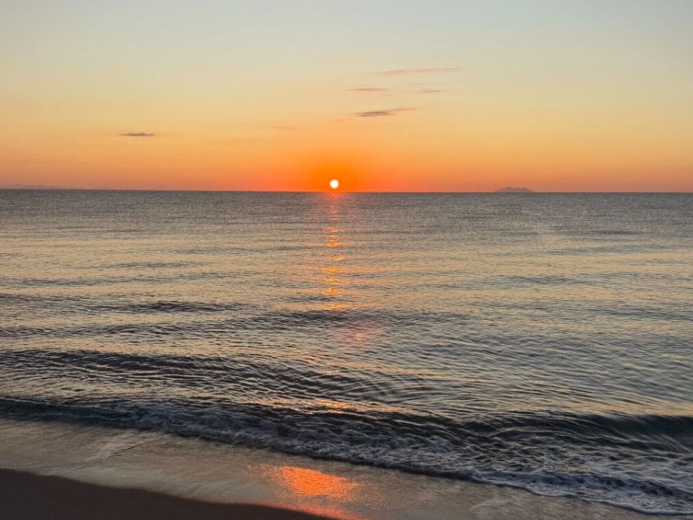 Un coucher de soleil sur une mer calme aux vagues douces.