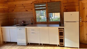 Eine kleine Küche mit Holzwänden, einem Spülbecken, einem Geschirrspüler, einem Kühlschrank und einem Fenster mit Jalousien.
