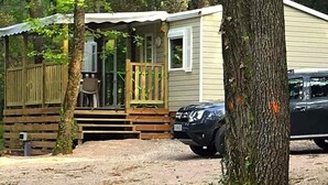 A small cabin with a porch, a car parked in front, and a dirt ground.