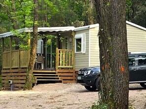 A small cabin with a porch, a car parked in front, and a dirt ground.