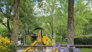 A playground with yellow equipment, surrounded by trees and purple flowers.