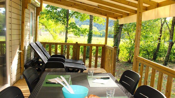 A covered outdoor dining area with a table set for two, chairs, a basket of bread, and a bowl with utensils.