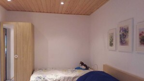 Une chambre avec deux lits, une armoire en bois et une porte donnant sur une autre pièce.