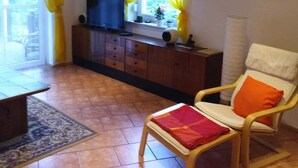Un salon avec une télévision, un canapé, un fauteuil et une fenêtre avec des rideaux.