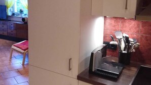 Une cuisine avec des meubles blancs, un plan de travail sur lequel se trouve une machine à café, et une fenêtre avec des rideaux.