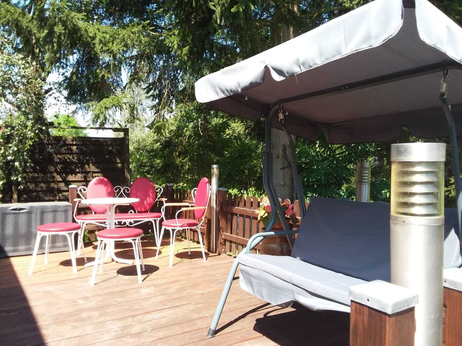 Een terras buiten met een overdekte zithoek, een tafel en stoelen.