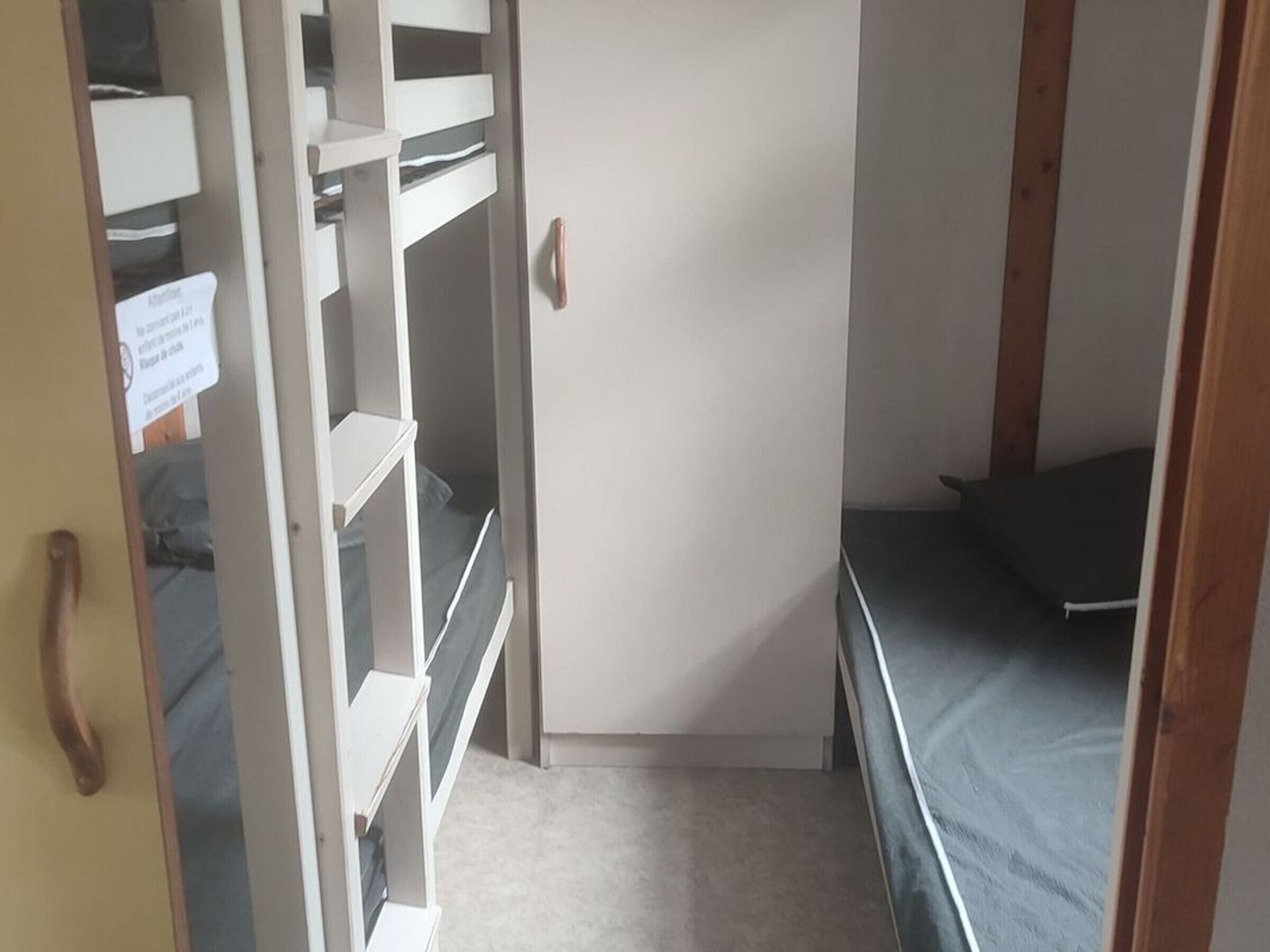 Habitación pequeña con literas, un escritorio y una puerta con un cartel.