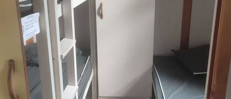 Habitación pequeña con literas, un escritorio y una puerta con un cartel.