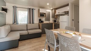 Un espacio habitable compacto con sofá, mesa de comedor, sillas, kitchenette y ventana con cortinas.