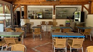 Un restaurante con interior de madera, suelo de baldosas y sillas de mimbre. Las mesas están dispuestas para comer.