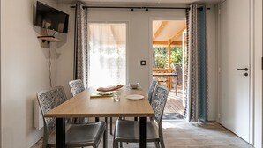Un comedor con una mesa de madera, cuatro sillas, un televisor de pantalla plana montado en la pared y vistas a una terraza exterior.