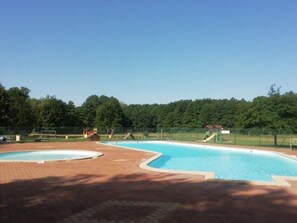 Une piscine entourée d’une clôture, un petit bâtiment et des arbres en arrière-plan.