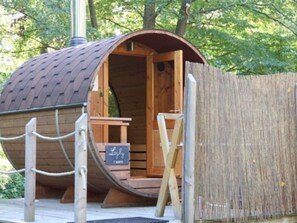 Une cabane en bois avec un toit incurvé, une porte en bois et un petit banc en bois à l’intérieur.