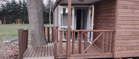 A wooden cabin with a porch, a staircase leading to the entrance, and a tree nearby.