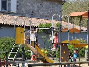 A playground with climbing structures and a slide, set against a stone building with a tiled roof. - Mobile home with AC, pets welcome - 4 guests (Vans)