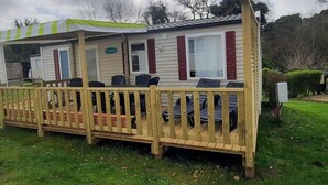 Una casa móvil con porche cubierto, un comedor con sillas y una pequeña terraza.