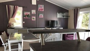 Cozinha compacta com mesa de jantar, cadeiras, televisão e janela com cortinas.