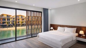 Une chambre d’hôtel avec un grand lit, une table de chevet, une lampe et une vue sur une piscine et des immeubles.
