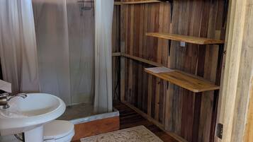 Ein Badezimmer mit Holzeinrichtung, einem weißen Waschbecken, einer Toilette, einer Duschvorhang und Holzregalen.