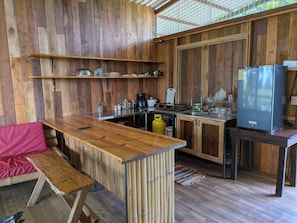 A rustic kitchen with wooden walls, a gas stove, a sink, and a refrigerator.