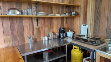 Eine kleine Küche mit Holzwänden, einer Edelstahl-Arbeitsplatte, einem Gasherd und verschiedenen Küchengeräten und Utensilien.