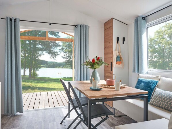 A modern room with a wooden table, chairs, a sofa, and a view of a lake. - Cozy mobile home, dog welcome - 4 guests (Luynes)