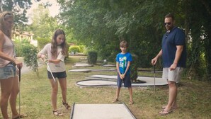 En gruppe mennesker spiller shuffleboard udendørs, med græs og træer i baggrunden.