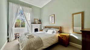 Ein Schlafzimmer mit einem großen Bett, einem Kamin, einem Nachttisch und einem Spiegel.