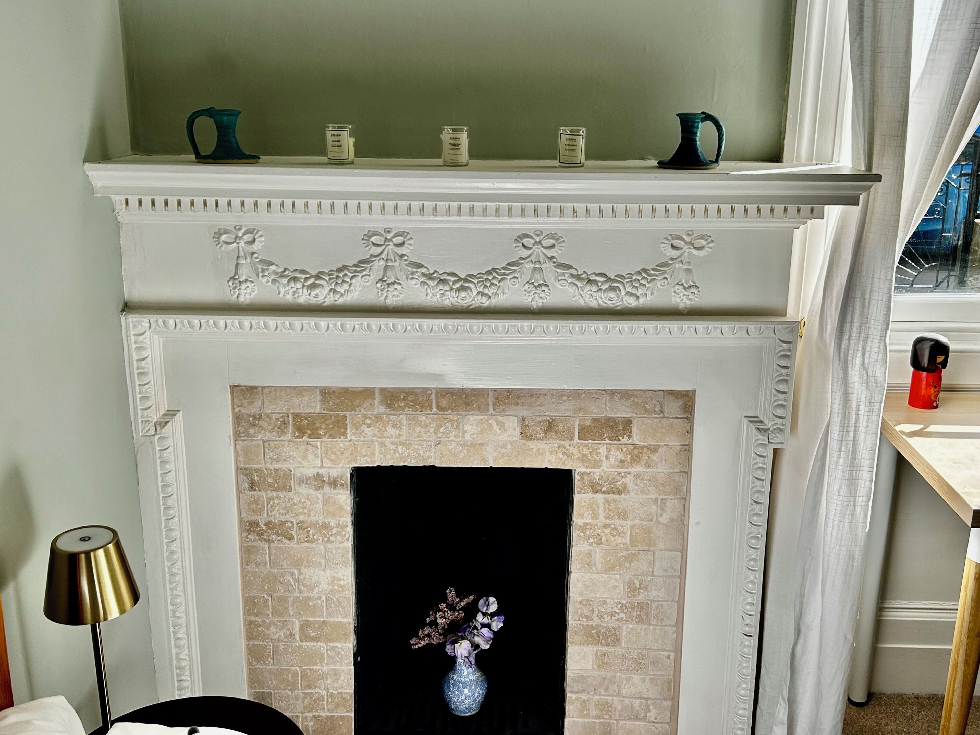 A fireplace with a brick surround, a white mantel with decorative carvings, and a vase with flowers on the mantel.