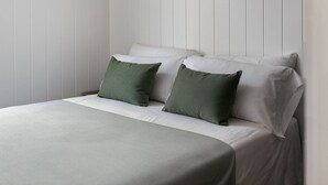 Un lit avec une literie blanche et deux oreillers verts, placé devant un mur blanc à panneaux.