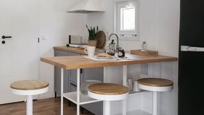 Une cuisine de taille réduite avec une table en bois, deux tabourets, une fenêtre et une porte blanche.