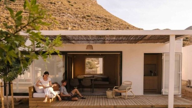 Un espace extérieur moderne aménagé avec une terrasse en bois, un coin salon couvert et une porte vitrée donnant accès à un espace intérieur.