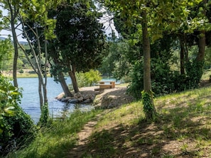 A lakeside path with a bench and a picnic table surrounded by trees.