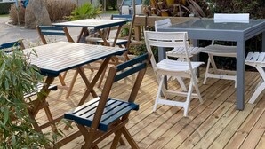 An outdoor dining area with wooden tables and chairs, a covered seating area, and a view of a residential area with houses and greenery. - Cozy mobile home - 2 guests (Perros-Guirec)