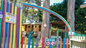 Un’area giochi con un arco ad arco, una casetta di legno e un cartello che indica divieto di accesso ai cani.