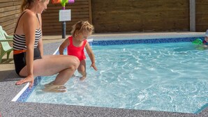 Un’area piscina con un muro di legno, una sedia verde e un giocattolo acquatico colorato.