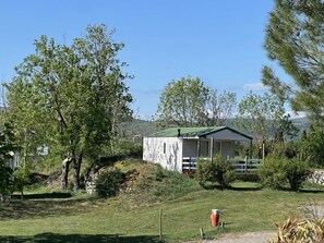 Ein kleines, eingeschossiges Gebäude mit grüner Dachbegrünung, umgeben von Bäumen und Gras, mit hügeliger Landschaft im Hintergrund.