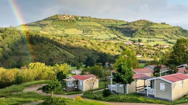 Paisagem rural com arco-íris, casas numa colina e um caminho que as leva.