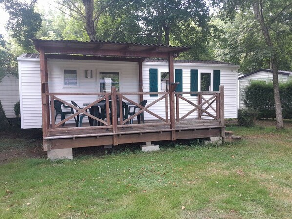 A small cabin with a wooden deck, green shutters, and a table with chairs. - Mobile home with air conditioning - 4 guests (Monplaisant)