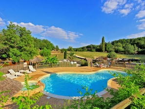 A swimming pool with lounge chairs, surrounded by a wooden fence and greenery.