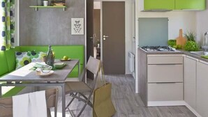 Una cocina moderna con armarios verdes, una zona de comedor con sofá verde, y una puerta visible que conduce a otra habitación.