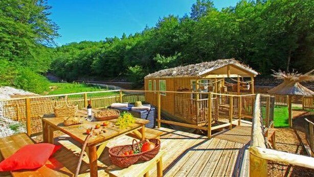 Una terraza de madera con mesas de picnic, una pequeña construcción de madera y un área cercada.