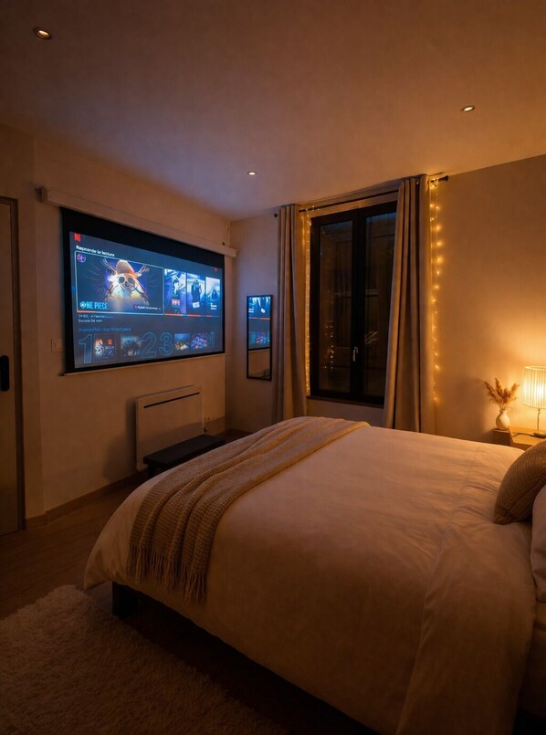 A bedroom with a large TV mounted on the wall, a bed with a blanket, a bedside table with a lamp, and a window with curtains.